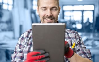 Un jeune homme, avec des lunettes de protection et des gants, qui utilise une tablette.