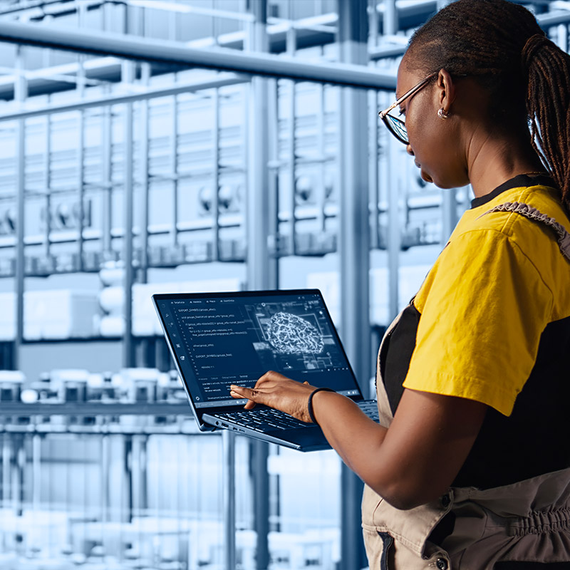 Marketing digital pour PME industrielle : prouver la qualité et accélérer la confiance Une jeune femme qui se trouve dans des locaux industriels avec un ordinateur portable entre les mains